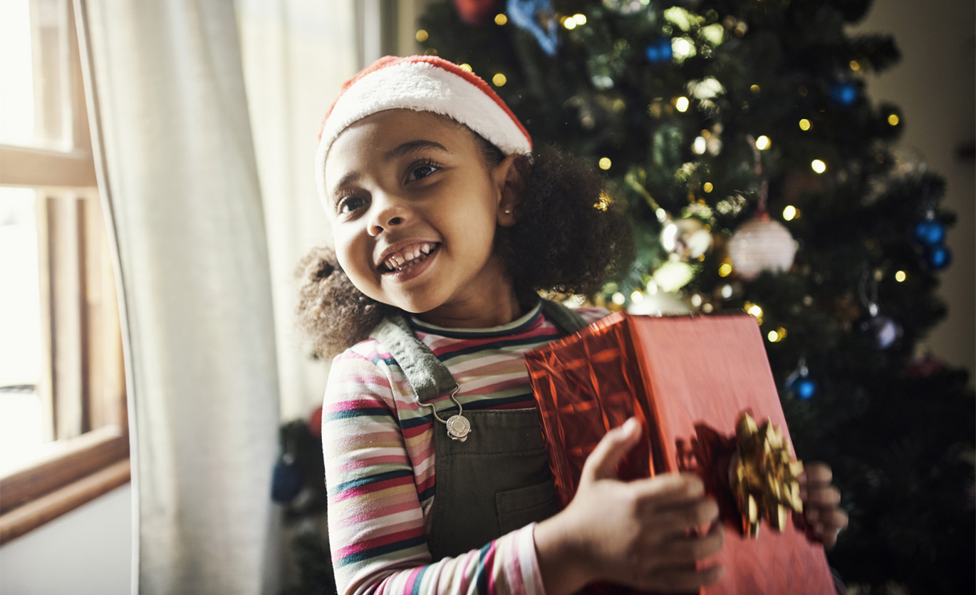young girl wearing a Santa hat and holding a Christmas present