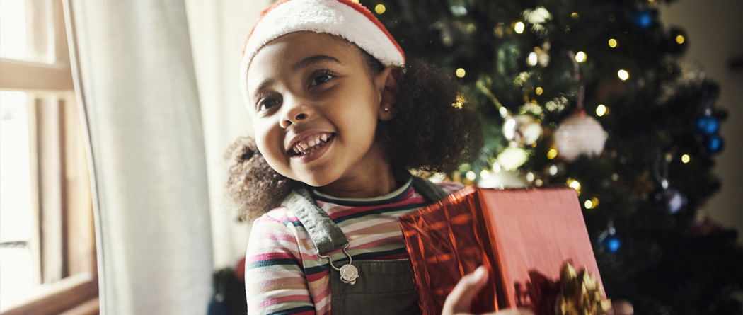 young girl wearing a Santa hat and holding a Christmas present